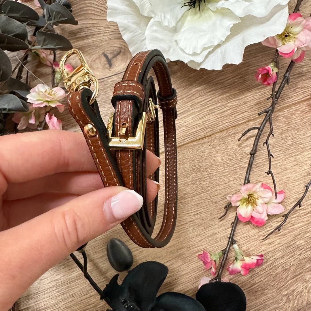 Hand holding an adjustable brown leather strap with gold buckle and clasp.