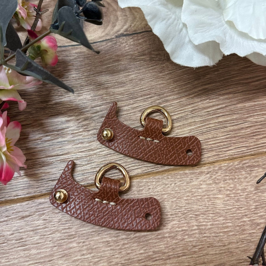 Brown leather D-ring tabs on wood beside flowers.